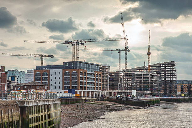 A view of a construction site in London, showing the development of new residential towers and office buildings. Cranes dominate the skyline as new buildings rise along the waterfront.