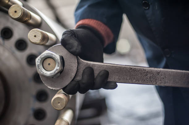 Mechanic repairman at the factory screws big bolt with large and heavy wrench key, holding it with both hands